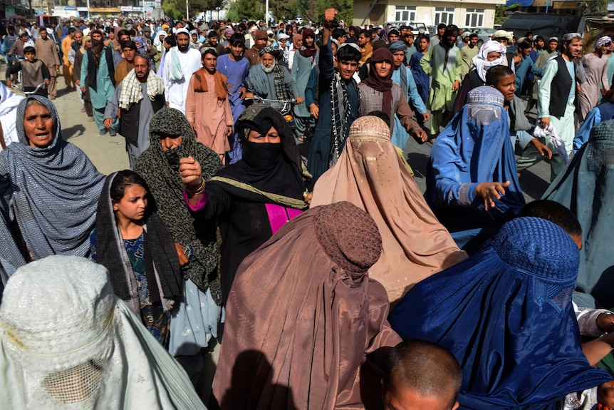 Women wearing burkas can be seen in a crowd of people. 