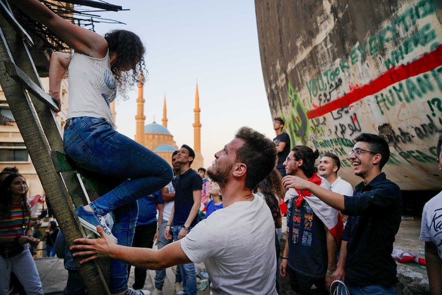 A young woman climbs down a ladder as men reach to help her