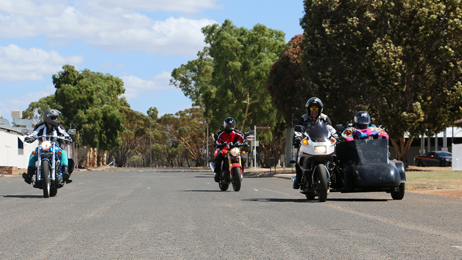 Three motorbikes ridden by members of the Barker family head towards the camera on a Wheatbelt road.
