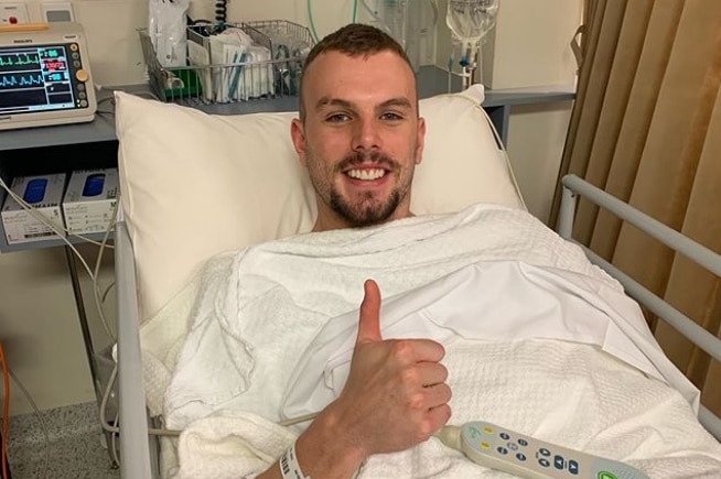 Olympic swimming champion Kyle Chalmers in a hospital bed giving the thumbs up.