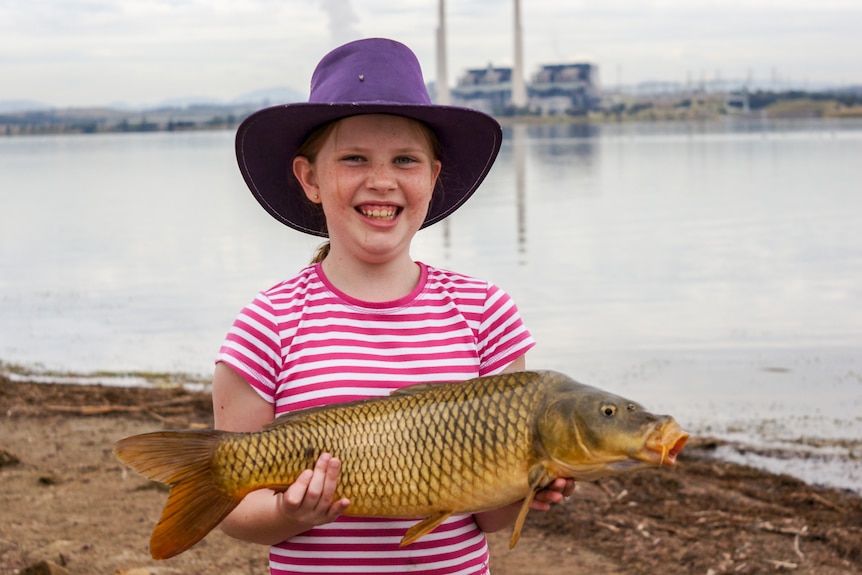 A young girl holds a carp.