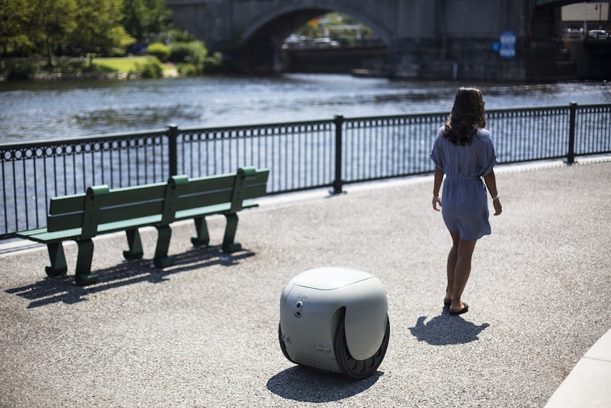A woman walks past a robot on a bridge near a river