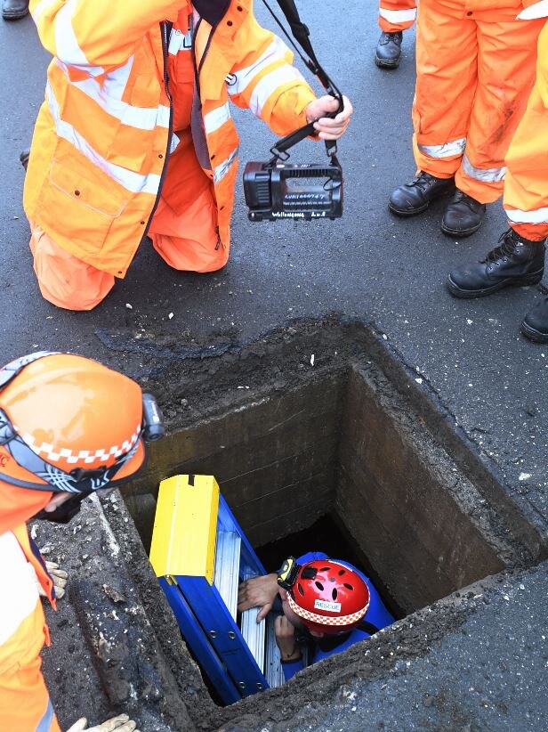 SES handing down a robotic camera to a worker in a drain
