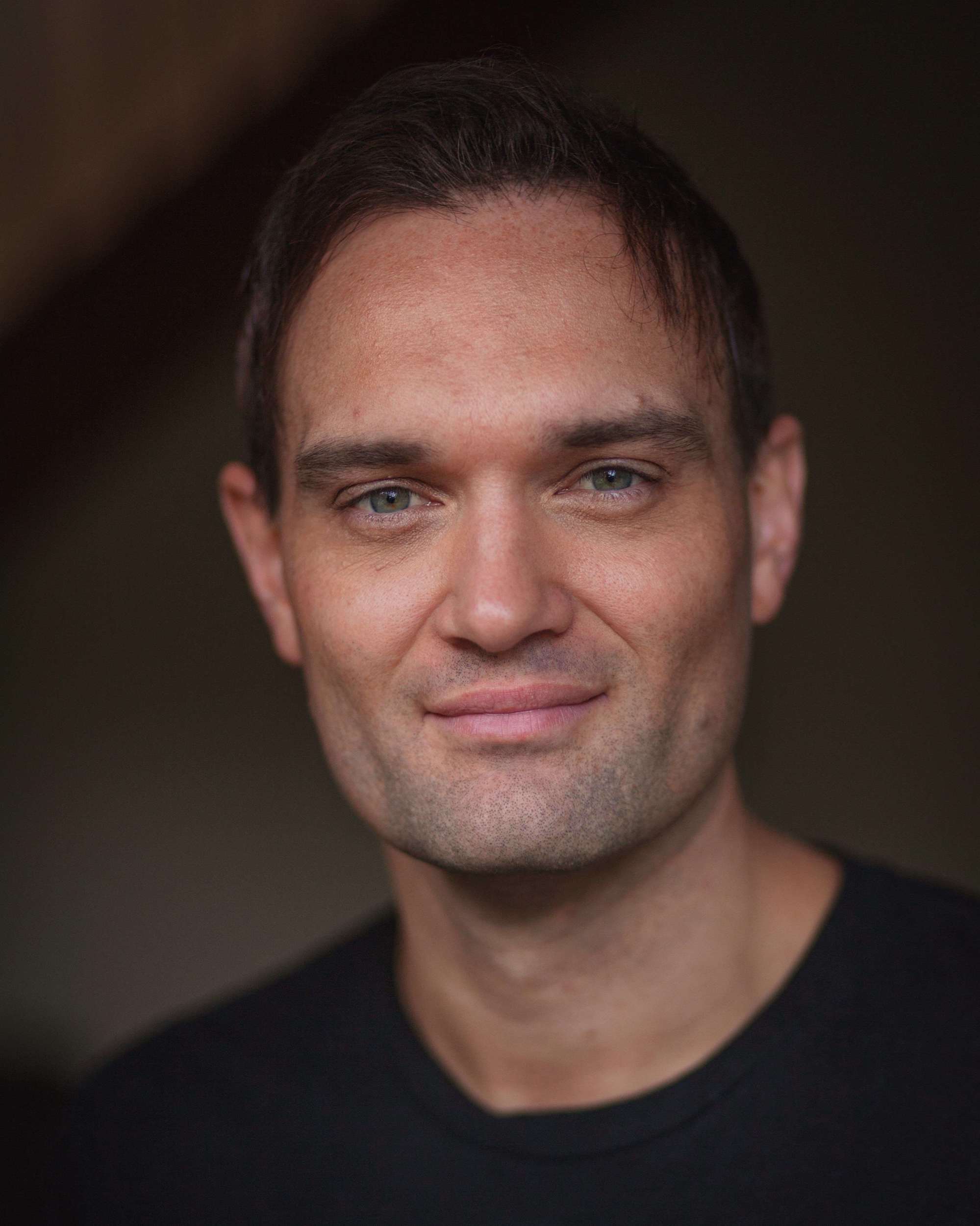 A headshot of Blake Erickson, a brunette white man in his 30s, wearing a black T-shirt.