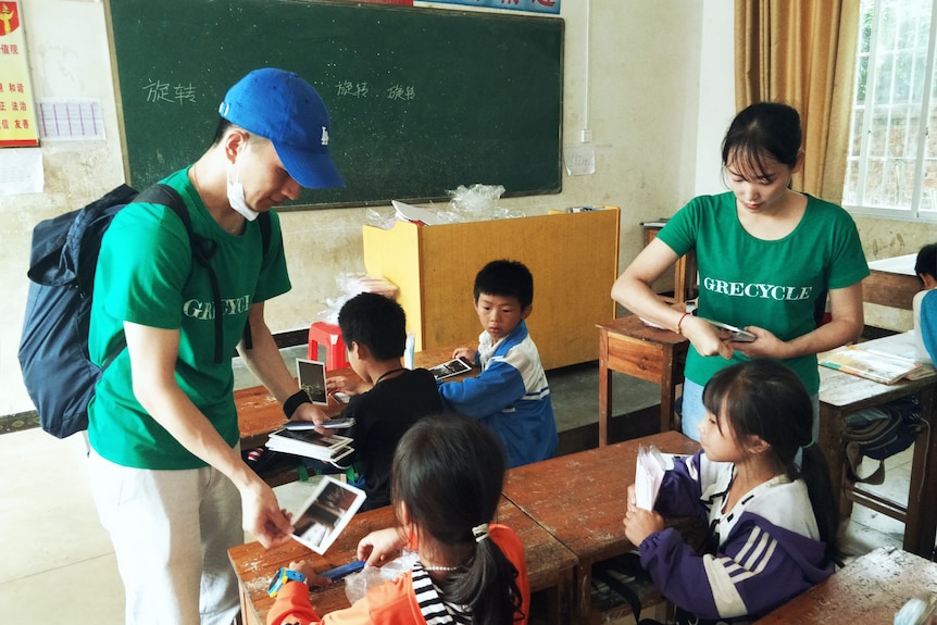 Two people in green shirt handing things to children. 
