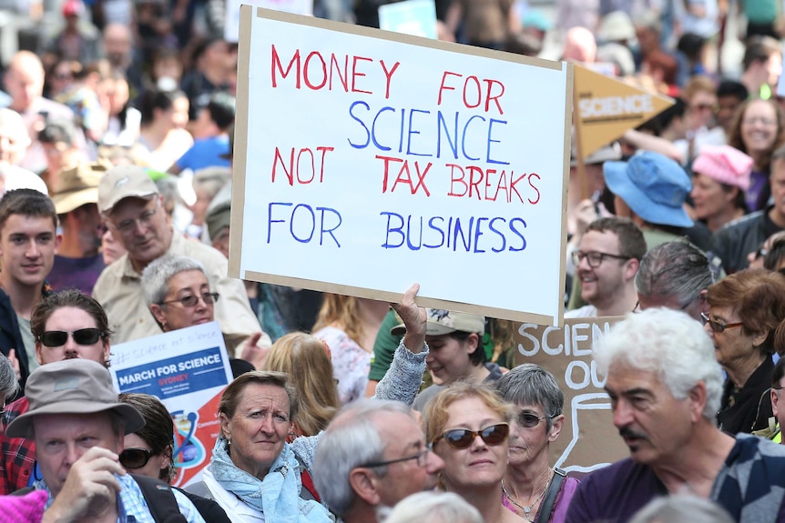 A woman holds up a placard in a crowd of people.