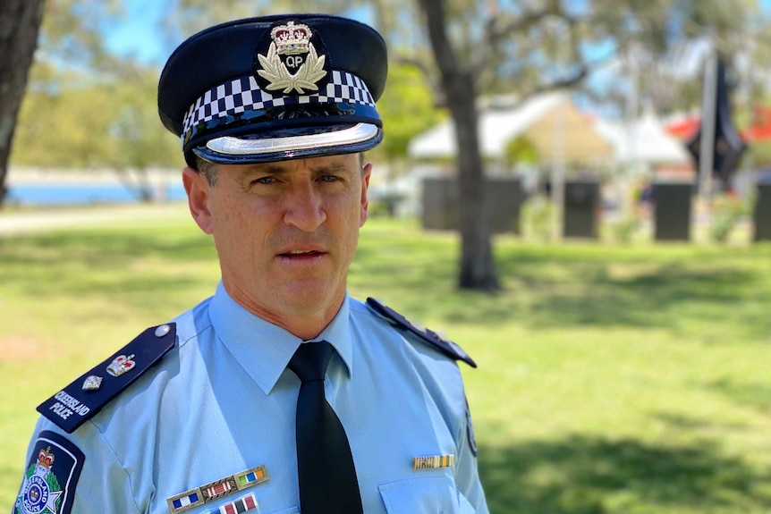 An older police officer in full uniform, giving a press conference outside on a sunny day.