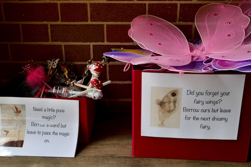 Two red boxes sit on the ground, filled with pink fairy wings and wands.