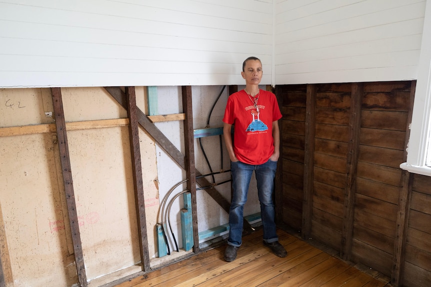 Jo Groves stands with her hands in her pockets, looking down, in front of an exposed wall with wires.