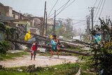 A woman with two small children walks past downed power lines and destroyed tin roofs.