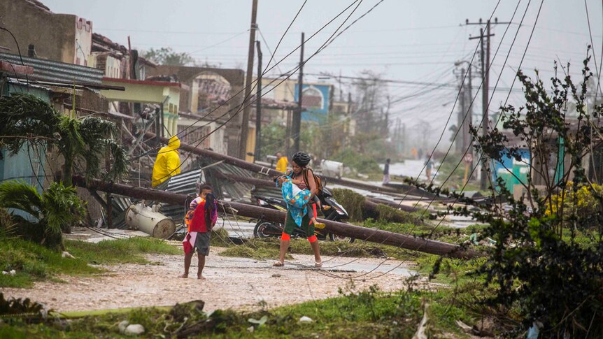 A woman with two small children walks past downed power lines and destroyed tin roofs.