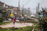A woman with two small children walks past downed power lines and destroyed tin roofs.