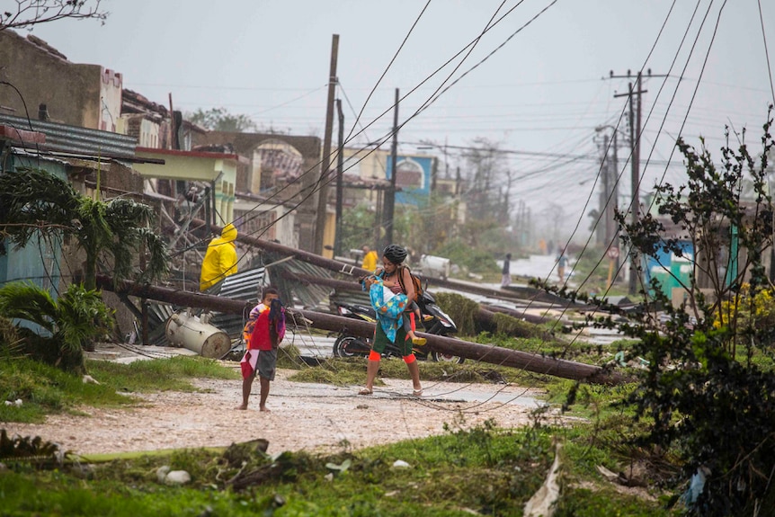 A woman with two small children walks past downed power lines and destroyed tin roofs.