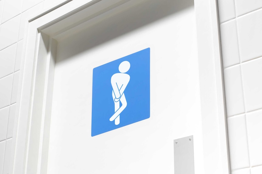 A white toilet door, surrounded by white tiles, is adorned with a blue sign featuring a white figure standing crossed legged.