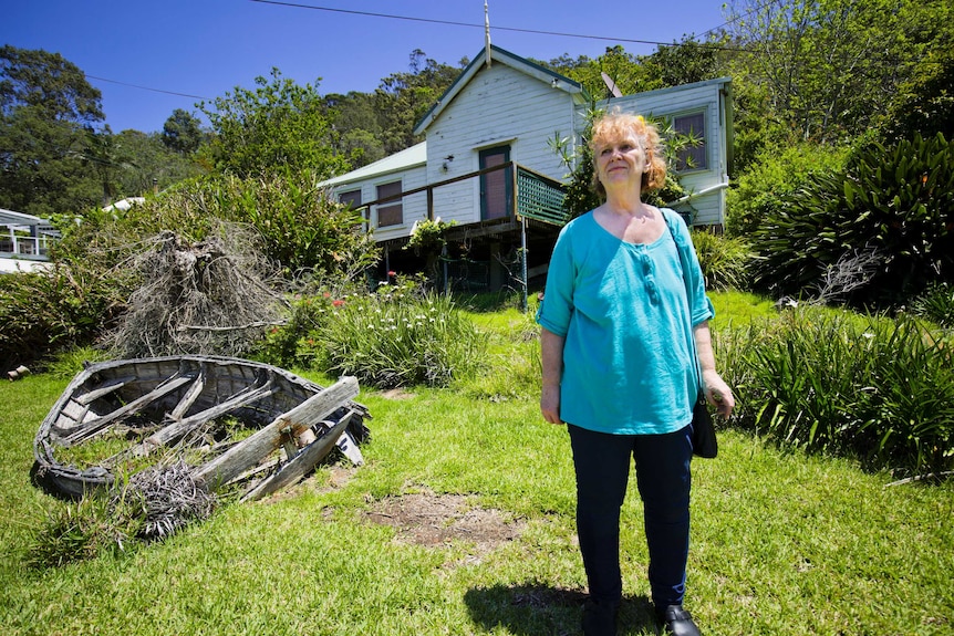 Marion Rae stands in front of a rundown cottage surrounded by bushland.