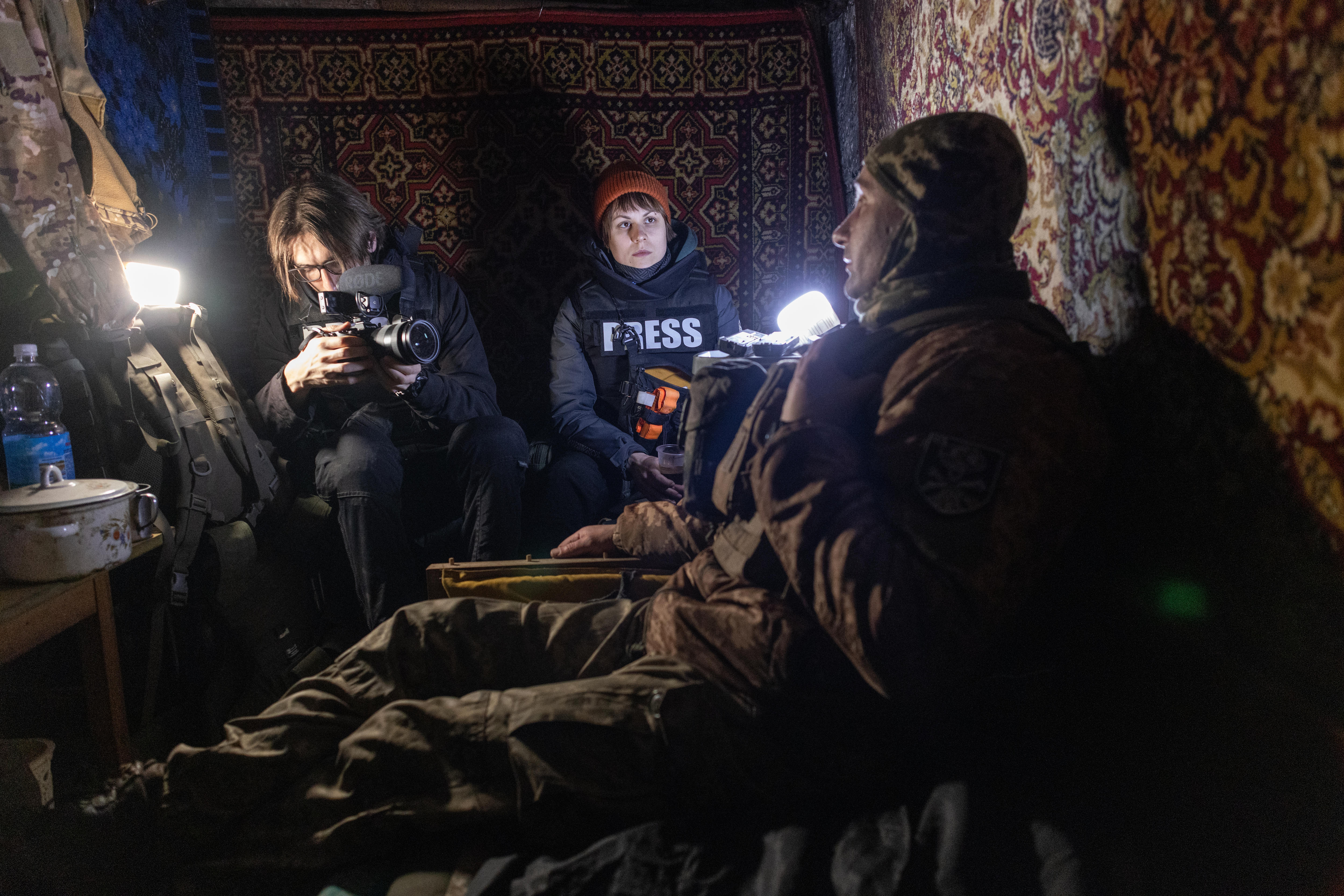 A reporter and cameraman film a soldier in the dark.