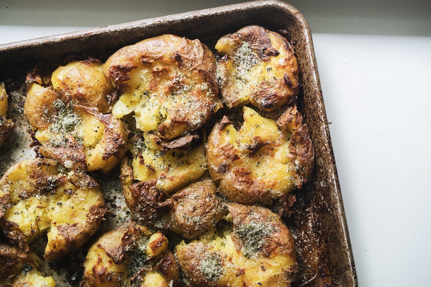 A close up of a baking tray with smashed baked potatoes sprinkled with seaweed salt, a perfect burger accompaniment.