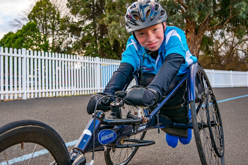 Boy sitting in his racing wheelchair smiling at the camera.