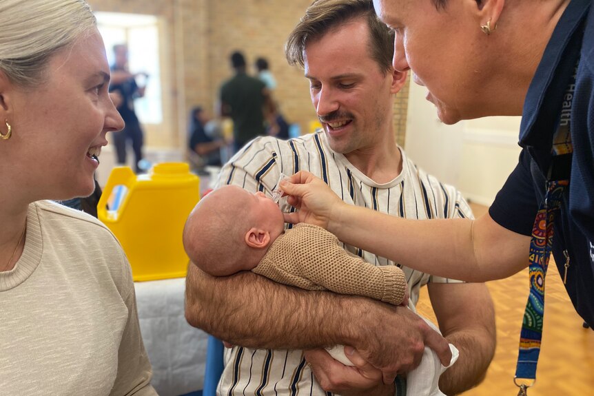 A man and a woman watch on as a nurse gives their baby son an oral vaccine.