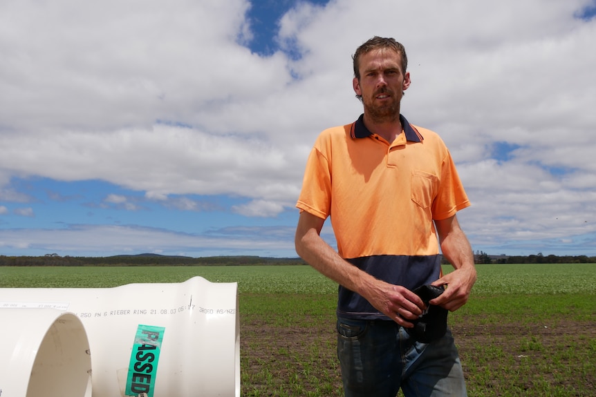 a farmer stands beside a pipe.