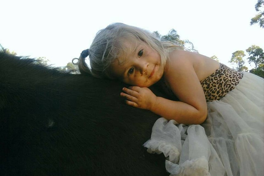 Kyanne on the back of a dark brown horse, resting her head on the side with her arm bent, wearing a cheetah and white dress.
