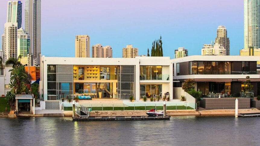 A picture of a large house with a canal in front of it and the Surfers Paradise skyline behind it.
