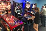 A young girl playing pinball next to a man