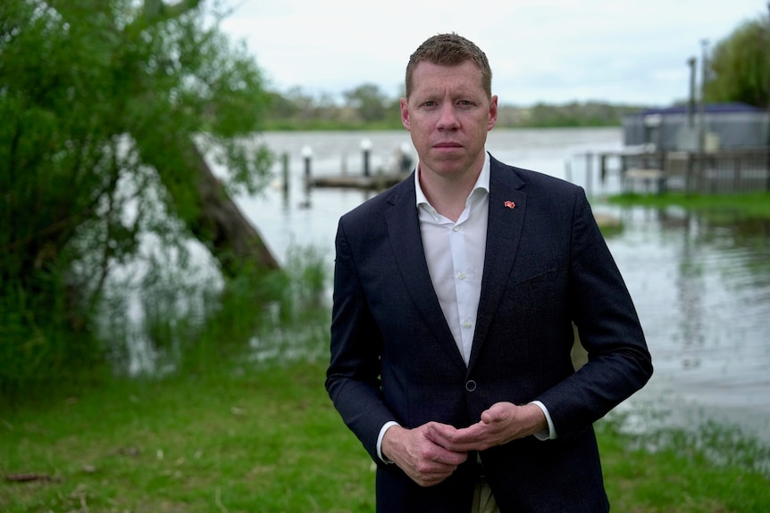 Man wearing a suit standing with a river behind him. 