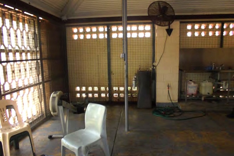 An undercover area in disrepair, with plastic chairs, fans, and an exercise machine.