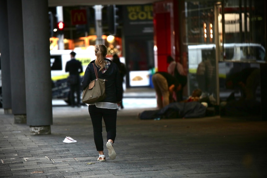 A woman walks on Hay Street in Perth's CBD and ahead of her are a group of rough-sleepers with sleeping bags on the footpath.