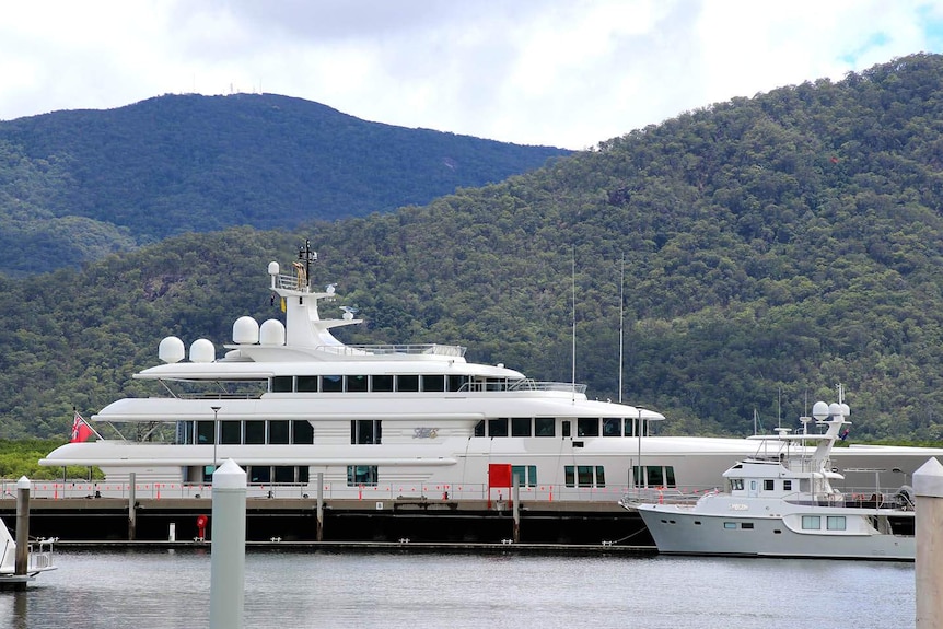 A superyacht moored at a marina with mountains in the background
