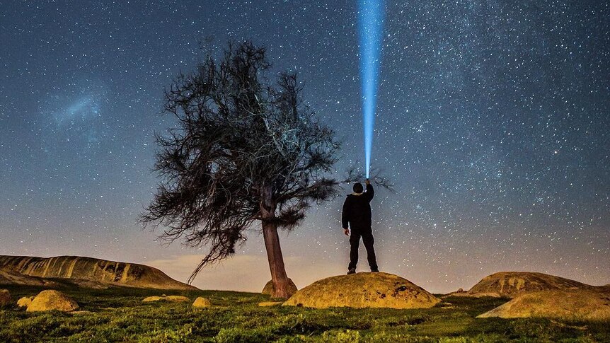 A person shines a torch up in to the starry sky.