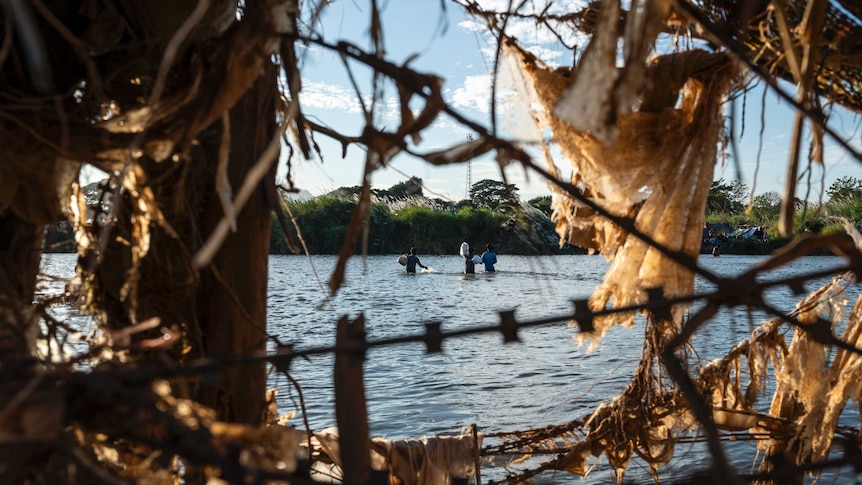 Refugees from Myanmar carrying bags of supplies while crossing the Moei river.