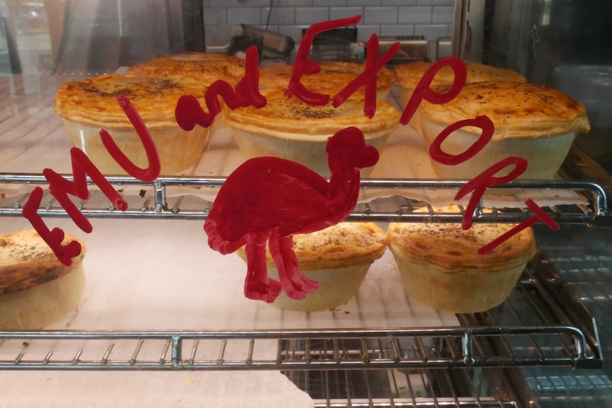 Pies sitting inside a pie-warmer daubed with the words 'Emu and Export', accompanied by a crude drawing of an emu.