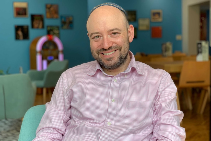 Dr Simon Holloway sitting in a blue room, with a jukebox, chairs and old records in the background.