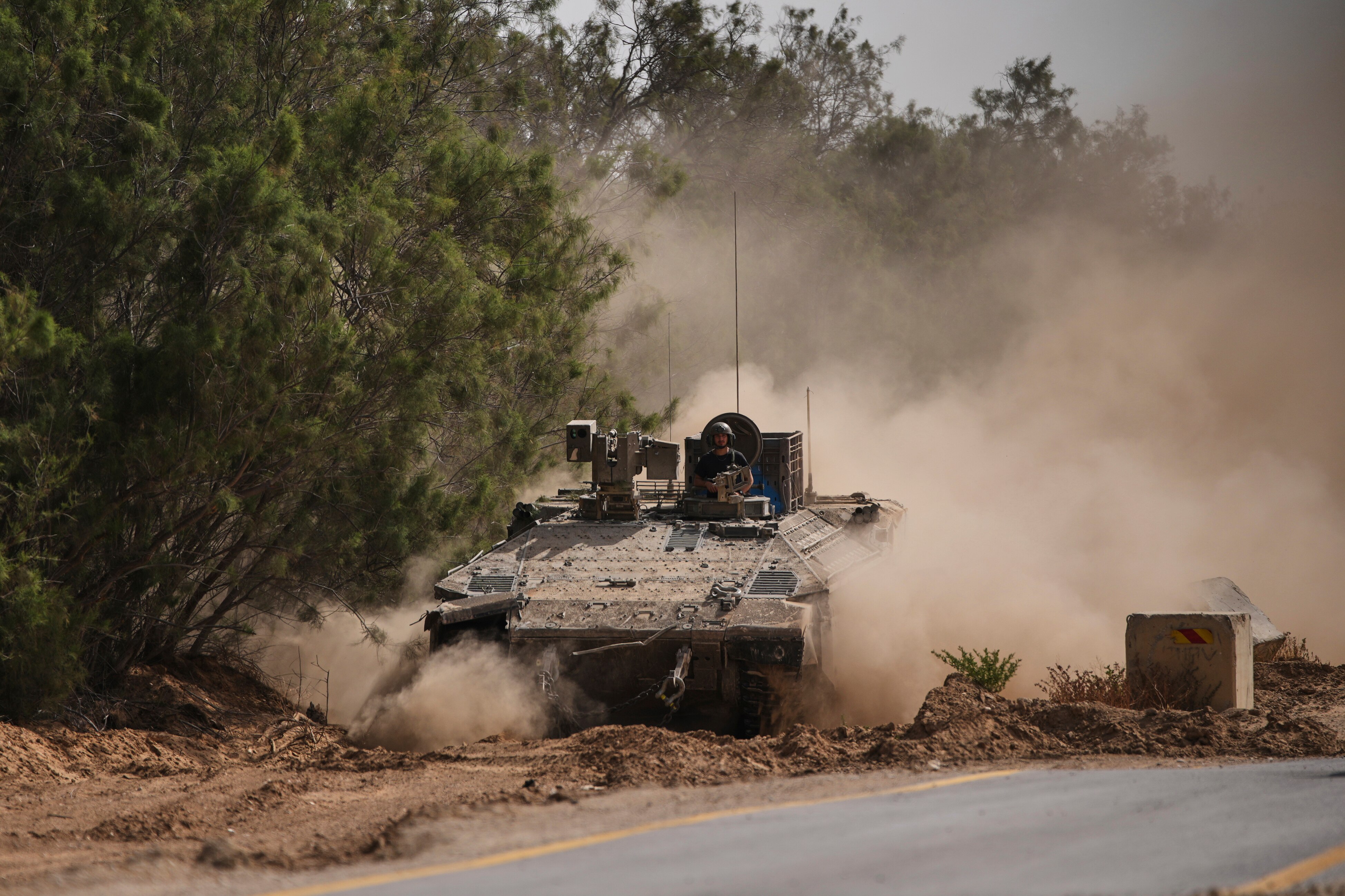 A large tank driving through a cloud of dust.