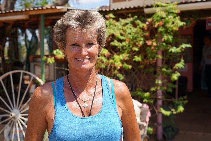 A woman smiles as she stands in front of a pub in a small town.