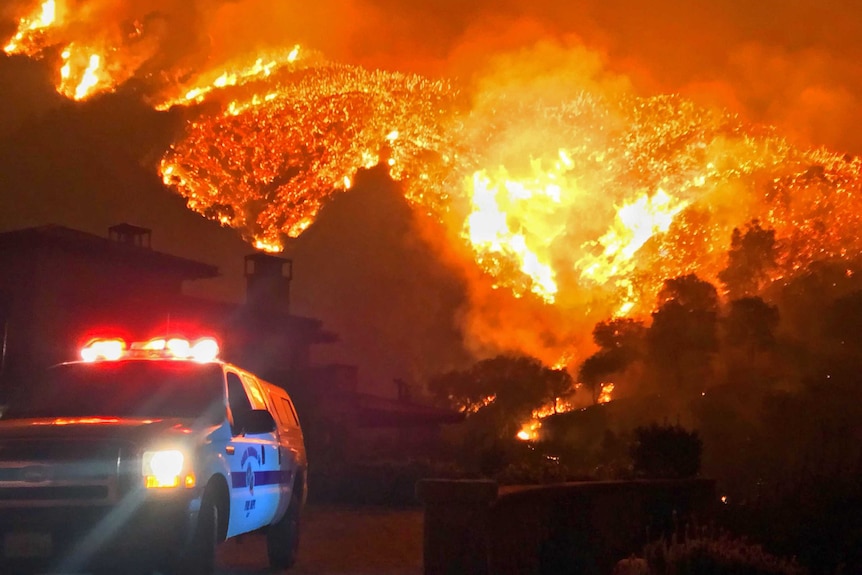 A police car sits running only metres away from a burning bushfire.