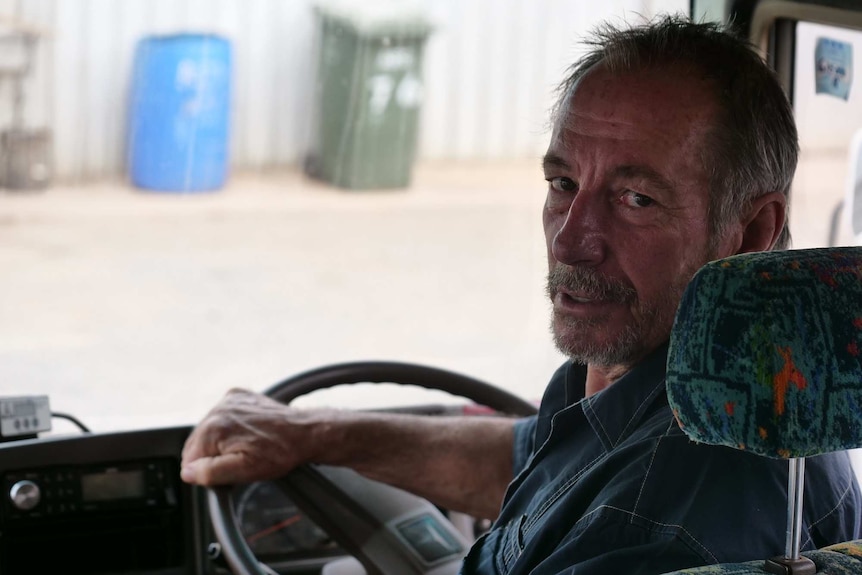 Grant Jaine, operator of the Bush Bee bus service, sits with his hands on the bus wheel and looks back at the camera