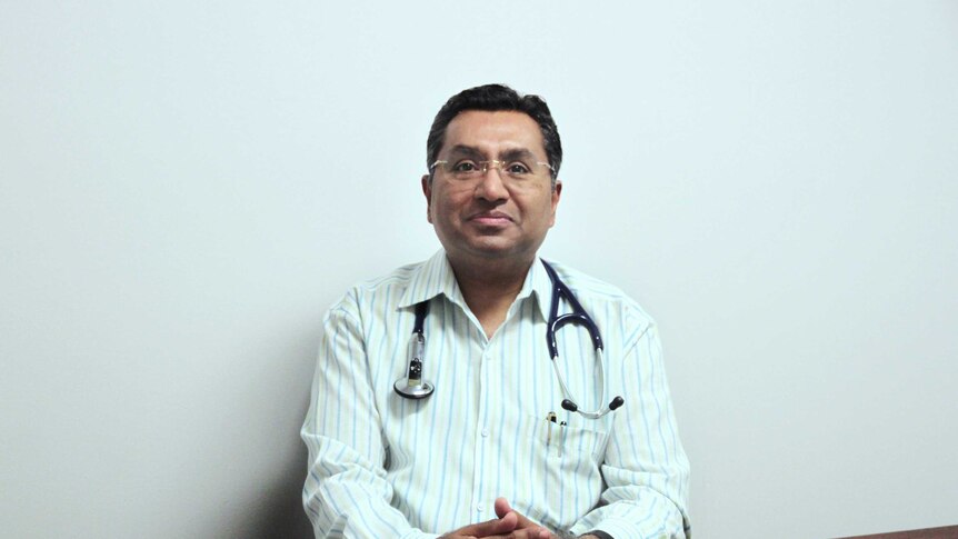 Smiling doctor sitting at table with hands clasped together.