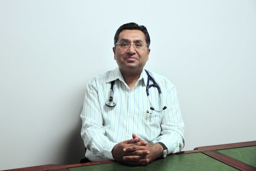 Smiling doctor sitting at table with hands clasped together.