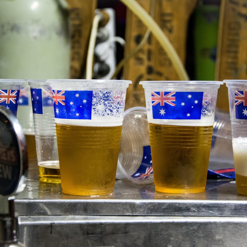 Four clear plastic cups of beer are lined up on a bar, each adorned with a picture of the Australian flag.