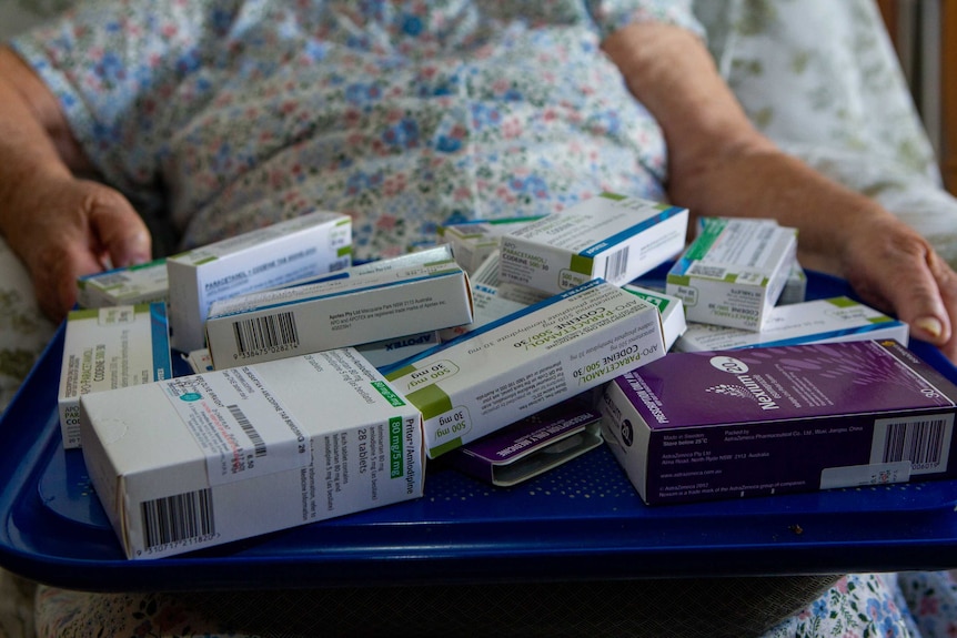 A pile of pharmaceutical drugs and opioids sits in the lap of an elderly person