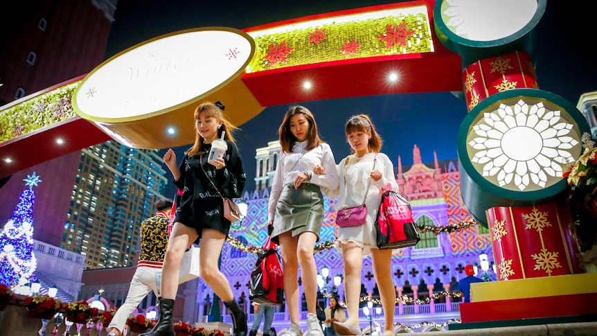Three young women walk down a set of stairs surrounded by fluorescent lights in Macau