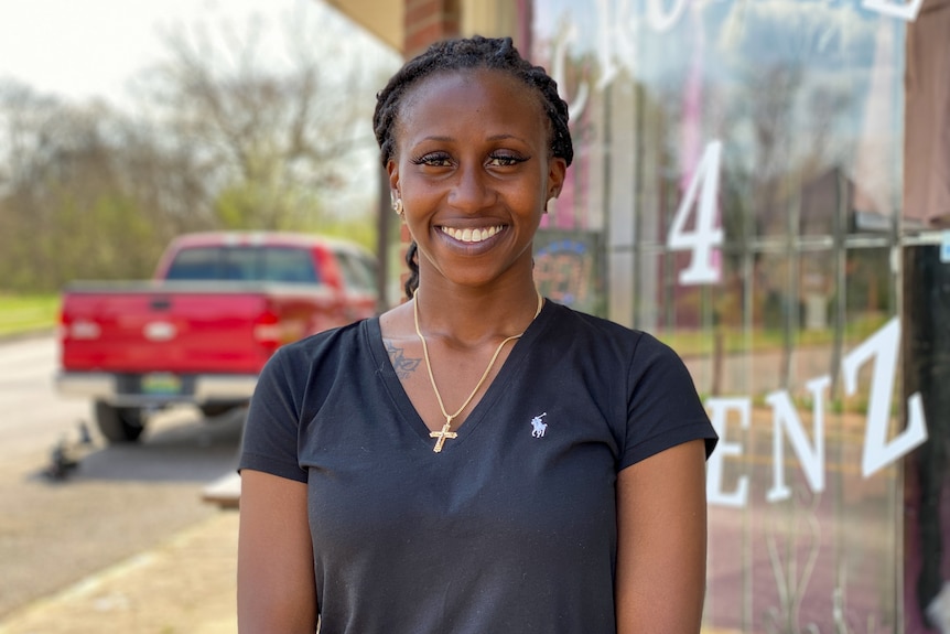 A woman in a blue T-shirt and a braid smiles at the camera