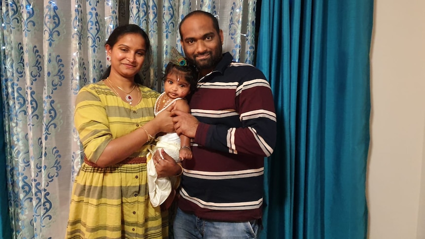 A wife and her husband smile as they hold their infant and pose for a photograph