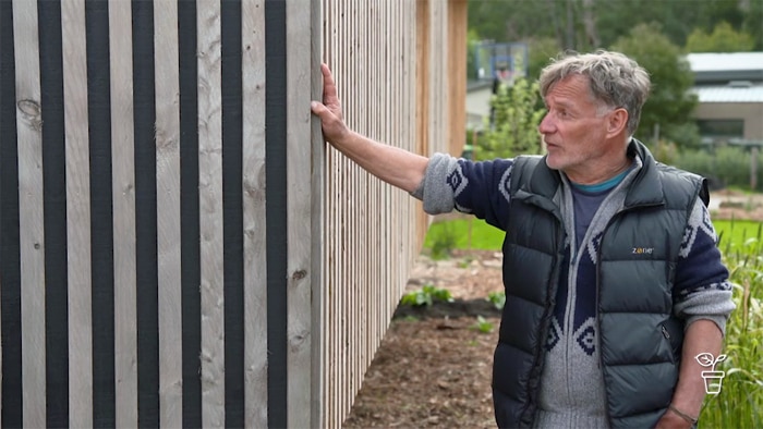 Man wearing vest with hand up against a timber fence