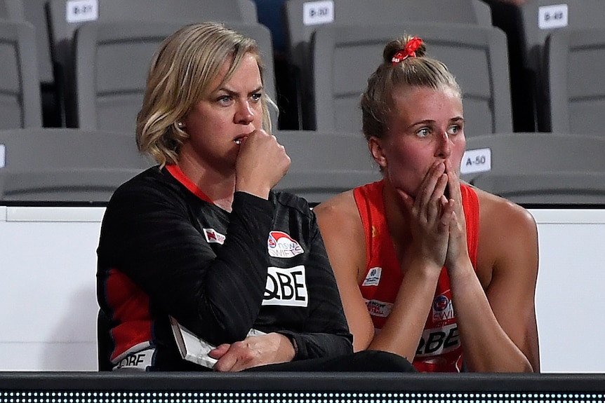 A concerned looking Super Netball coach and one of her players watch the court during a game.