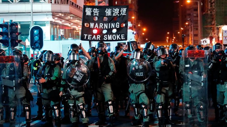 Police man shielded and with tear smoke in a protest in Hong Kong.