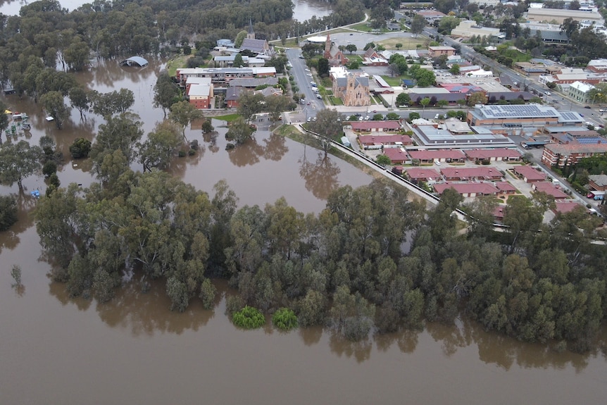 An aerial shot of a swollen river on the edge of a rural city.